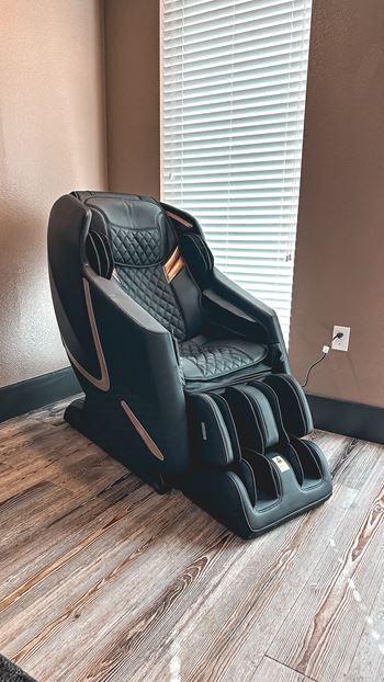 A black massage chair with a wooden base is placed in a room.